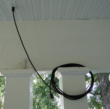 Electrical outlet in ceiling with cord coild on porch post edge.